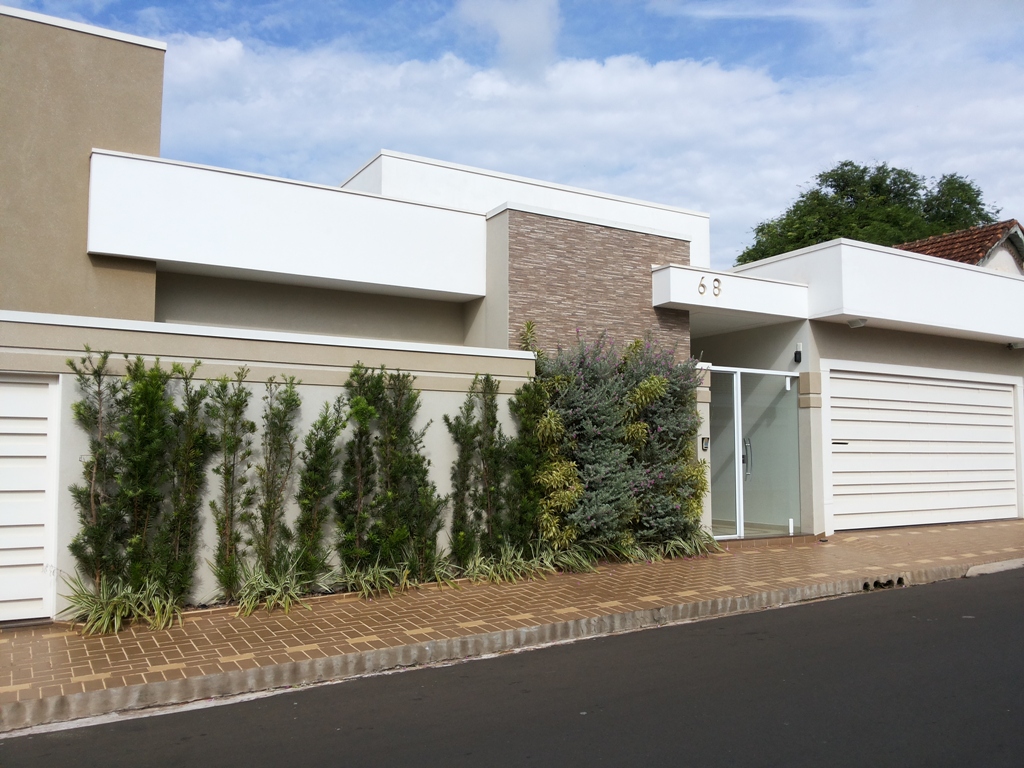 Residência contemporânea - Fachada em volumes brancos e revestimento em pedra, com jardim vertical acompanhando o muro e cobertura plana.