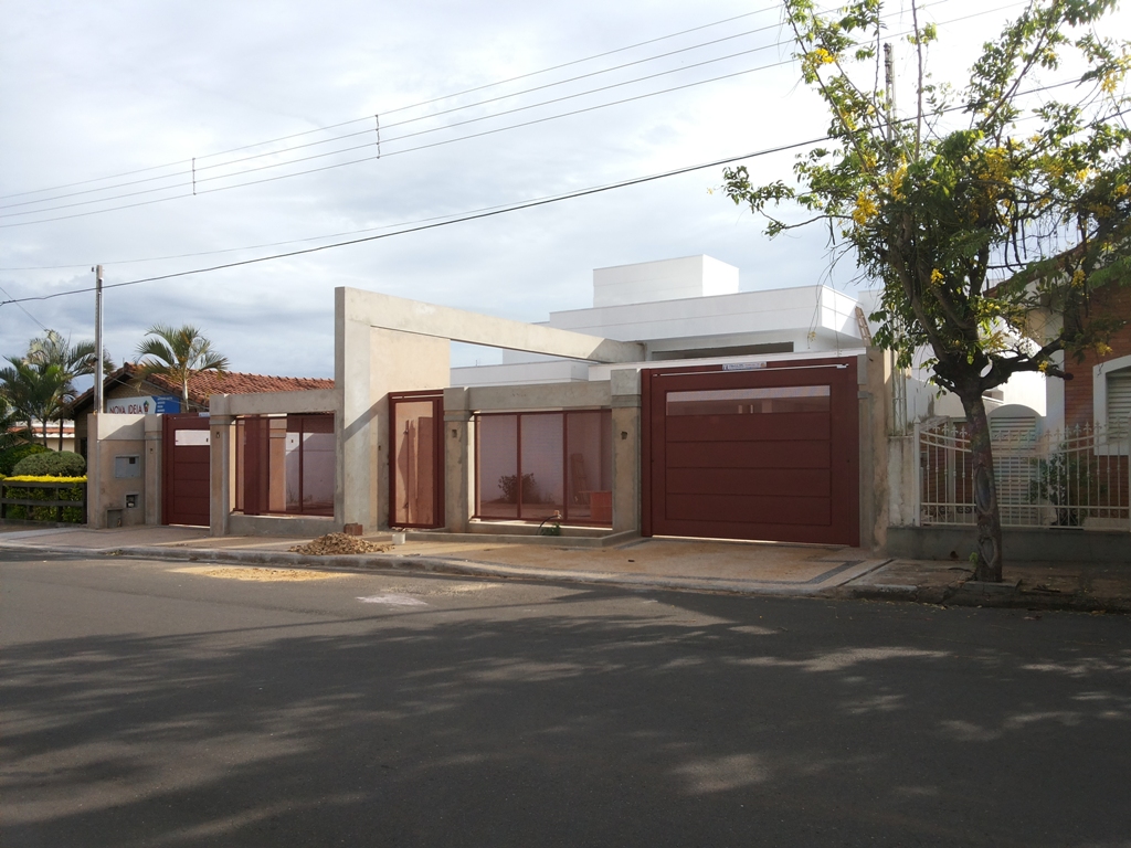 Residência com pórtico - Pórtico de concreto aparente marcando a entrada, esquadrias em tom vinho e recuo ajardinado.
