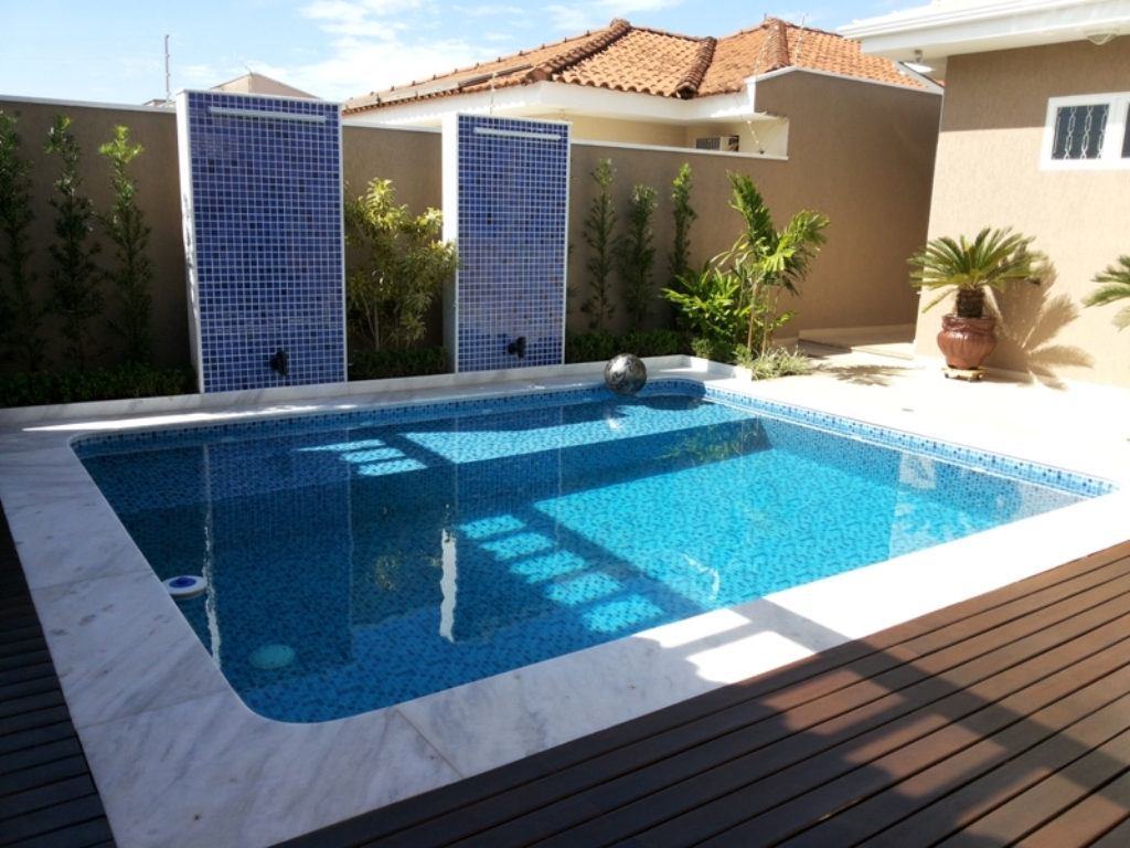 Piscina e deck de madeira - Painéis de pastilha azul, borda em mármore e deck de madeira integrando a piscina ao quintal.