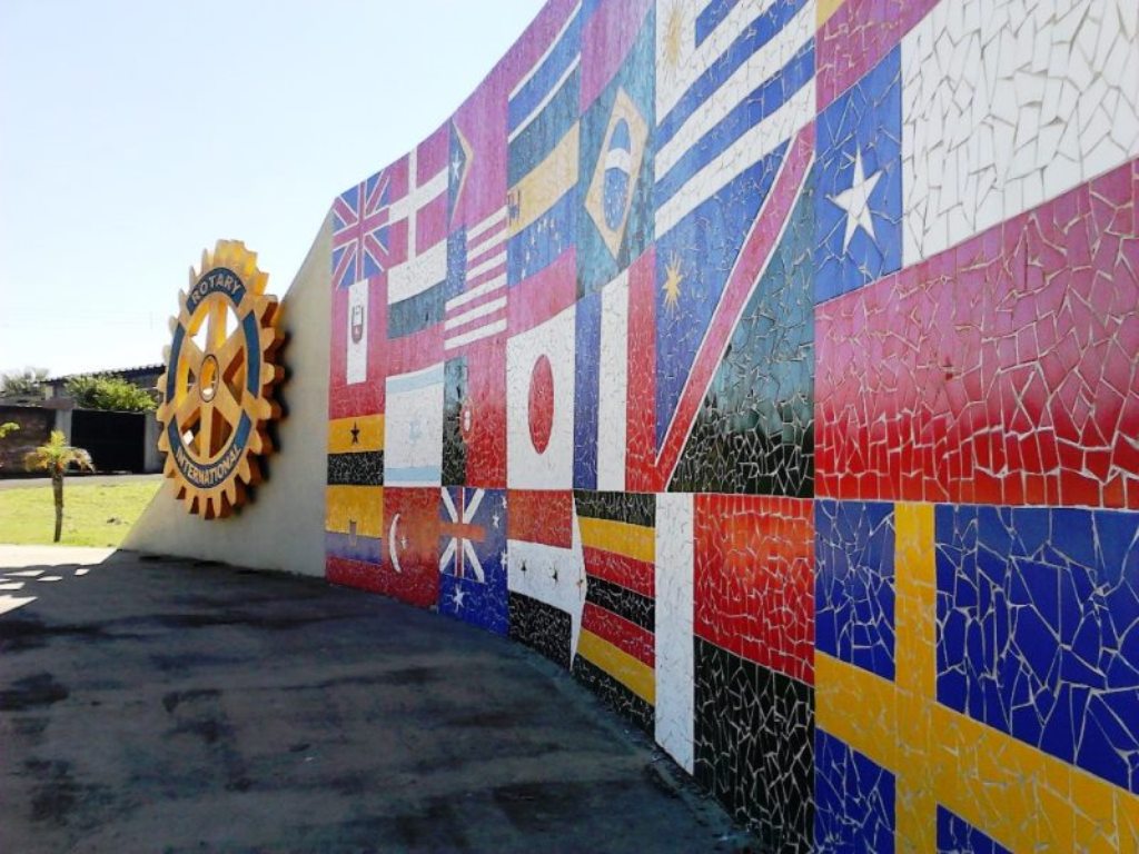 Monumento em mosaico - Muro curvo revestido em mosaico com bandeiras e emblema, marcando um espaço público da cidade.